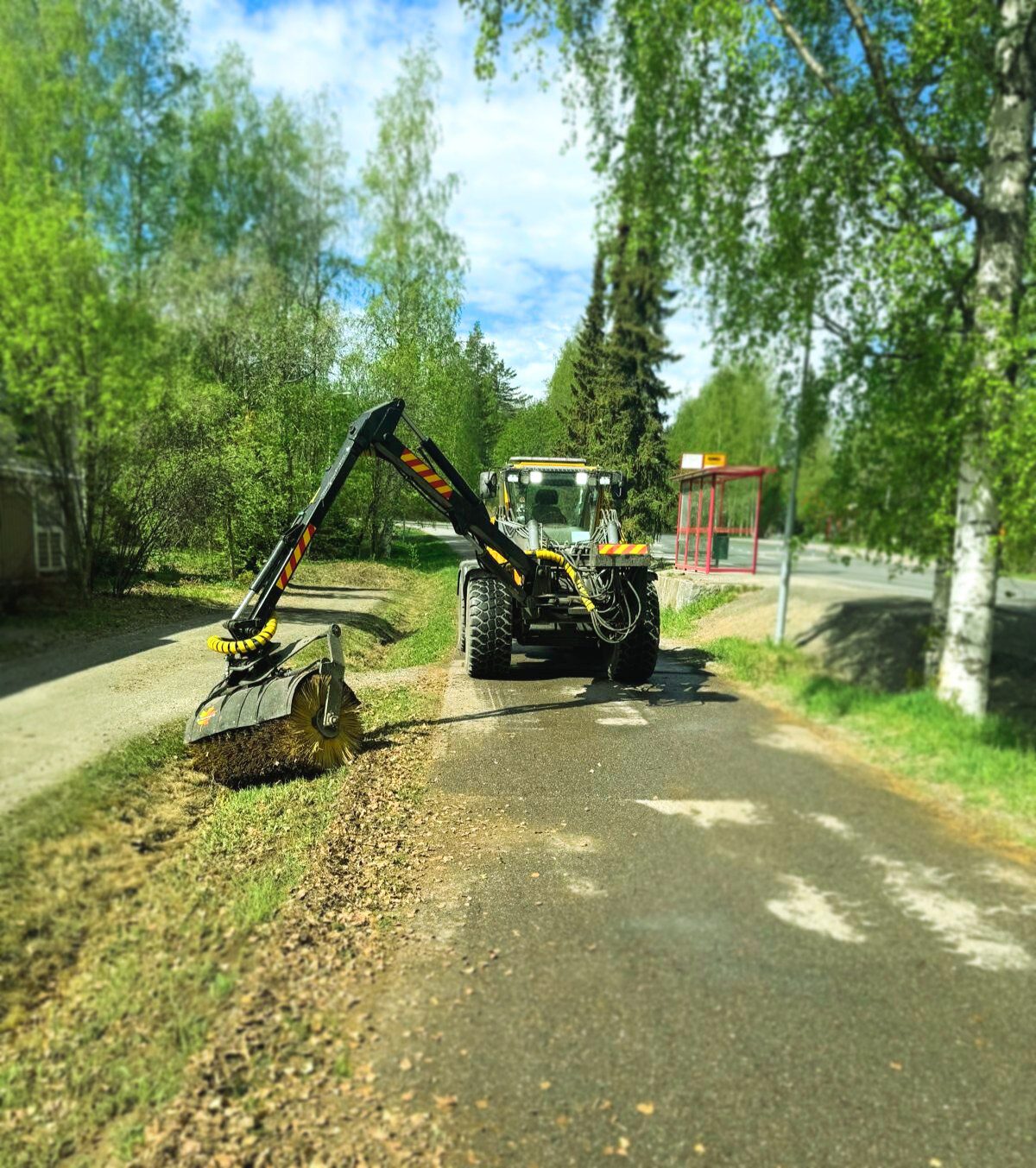 Keltainen ja musta kadunlakaisuauto, osa kunnossapidon ja koneurakointipalveluiden kokonaisuutta, puhdistaa nurmikon ja puiden reunustaman päällystetyn polun reunaa aurinkoisena päivänä. Taustalla lähellä tietä näkyy punainen linja-autopysäkkikatos. , JR Pihahuolto Oy Kuopio Keltainen ja musta kadunlakaisuauto, osa kunnossapidon ja koneurakointipalveluiden kokonaisuutta, puhdistaa nurmikon ja puiden reunustaman päällystetyn polun reunaa aurinkoisena päivänä. Taustalla lähellä tietä näkyy punainen linja-autopysäkkikatos. , JR Pihahuolto Oy Kuopio